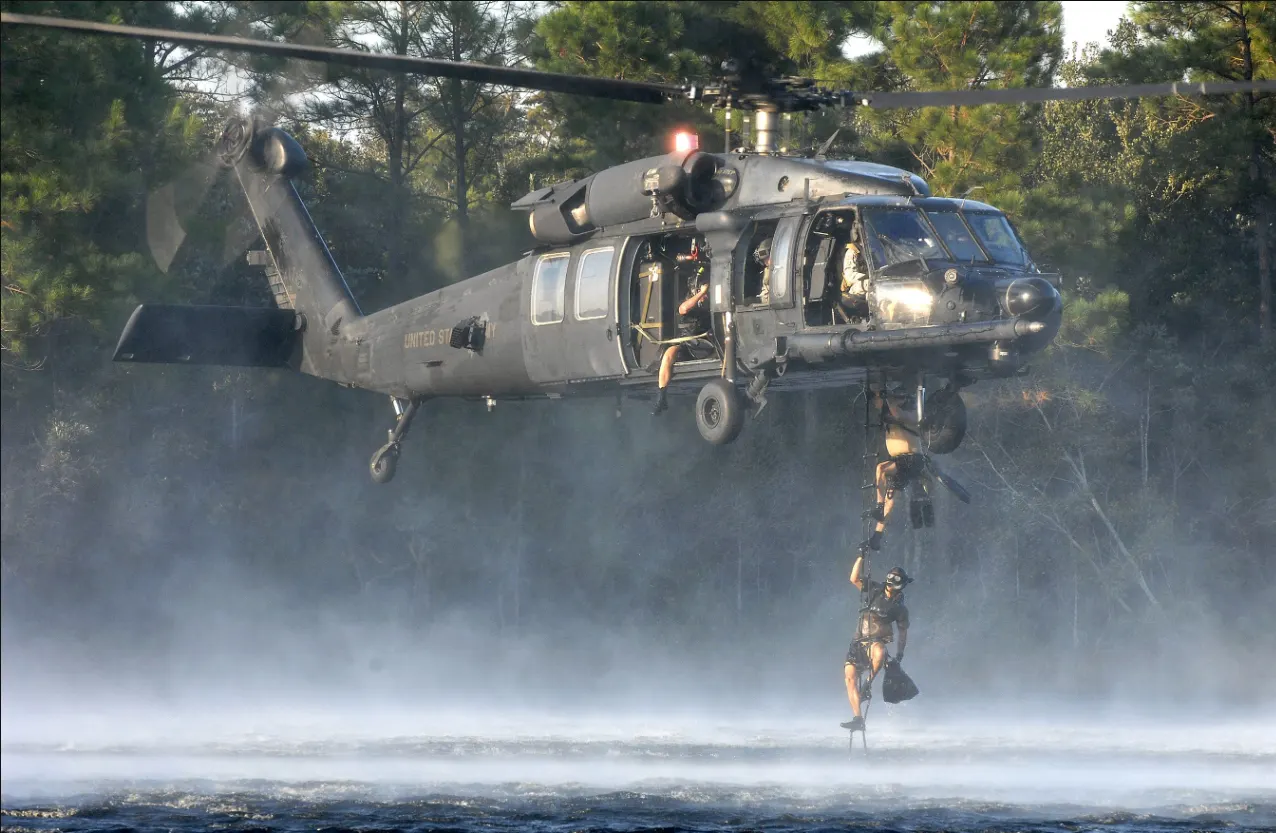 A pararescueman climbs a rope ladder from the water into a hovering U.S. Air Force rescue helicopter